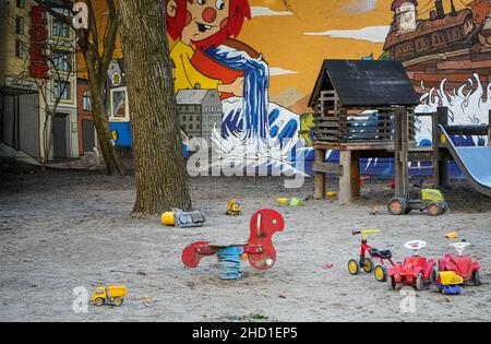 Kinderspielplatz in einer Stadt, mit zahlreichen Spielsachen, Sandkasten und Rutsche vor einer Wand mit bunten Straßenkunst Stockfoto