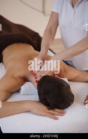 Vertikale Aufnahme einer nicht erkennbaren professionellen Masseurin, die im Spa arbeitet, entspannender Hals eines Klienten mit Massage Stockfoto