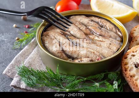 Sprotten in einer offenen Blechdose, in Reihen gestapelt, Brot, Kräuter, Zitrone, Frische Tomaten auf einem betonierten Hintergrund. Zutaten für Smorrebrod. Stockfoto