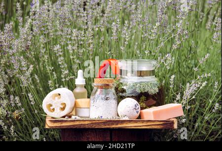 Verschiedene Lavendel-Spa-Produkte auf Holztablett im blühenden Lavendelfeld am sonnigen Sommertag. Glaskanne gefüllt mit heißem Lavendeltee-Getränk. Stockfoto