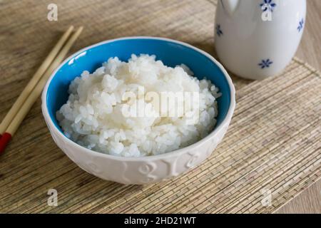 Japanischer Uruchimai-Reis in einem hübschen Keramikschüssel mit Essstäbchen gedämpft Stockfoto