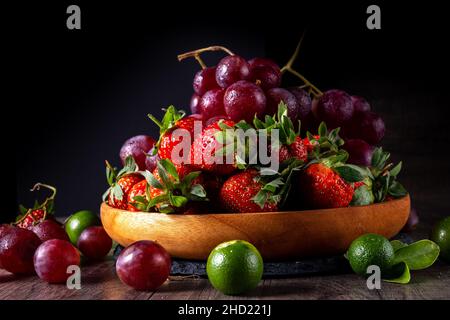 Trauben und Erdbeeren und in einem Behälter aus Holz, mit ein paar Stück Limette auf dunklem Grund Stockfoto