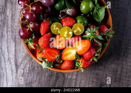 Trauben und Erdbeeren und in einem Behälter aus Holz, mit ein paar Stück Limette auf dunklem Grund Stockfoto