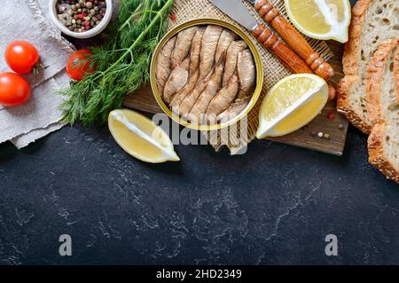 Geräucherte Sardinen in einer offenen Blechdose, knuspriges Vollkornbrot, Gemüse, Zitrone, frische Tomaten. Draufsicht, flach liegend. Food-Hintergrund mit Kopierplatz. Stockfoto