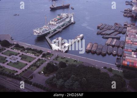 Yamashita Park & Hikawamaru vom Marine Tower, Yokohama, Japan, einschließlich des Weißen Leuchtturms und des Sea Bus Pier. Auch viele Lastkähne. August 1977 Stockfoto