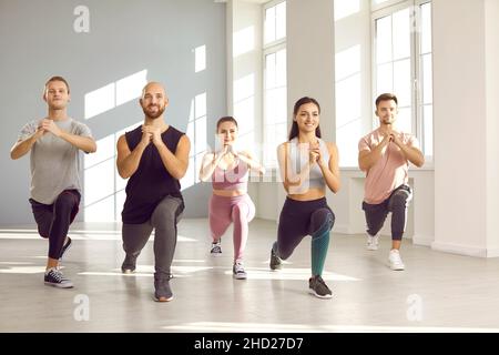 Junge aktive Menschen im Gruppentraining führen gemeinsam Beinübungen im hellen Fitnessstudio durch. Stockfoto