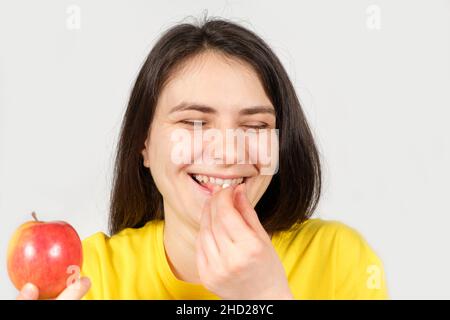 Eine glückliche gesunde Frau lacht und nimmt eine Vitaminpille oder ein Nahrungsergänzungsmittel, während sie einen Apfel in der Hand hält Stockfoto