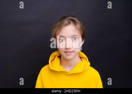 Ein gutaussehender, lächelnder junger europäischer Teenager, der sprachlos auf die Kamera schaut, schockiert durch hohe Preise, trägt einen lässigen, leuchtend gelben Hoodie, der auf blauem Hintergrund isoliert ist Stockfoto