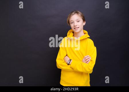 Ein gutaussehender, lächelnder junger europäischer Teenager, der sprachlos auf die Kamera schaut, schockiert durch hohe Preise, trägt einen lässigen, leuchtend gelben Hoodie, der auf blauem Hintergrund isoliert ist Stockfoto