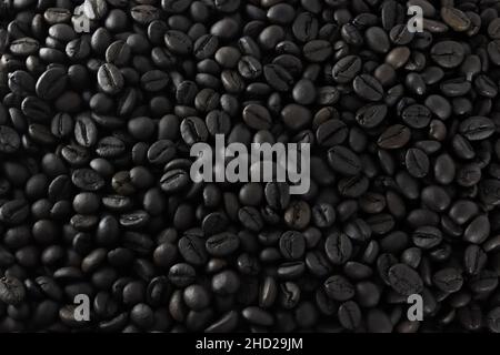 Textur von gerösteten Kaffeebohnen. Dunkler Hintergrund mit einer Spiegelung von hellem Licht auf Kaffeebohnen. Das beliebteste Getränk der Welt. Stockfoto