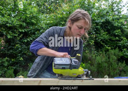 Junge Frau mit elektrischen Power-Sägewerkzeug ohne Sicherheits-Googles oder Schutzkleidung - Modell freigegeben Stockfoto