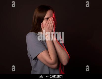 Eine junge Frau versteckt sich und bedeckt ihr Gesicht mit Händen, Handflächen in Angst oder Frustration. Stockfoto