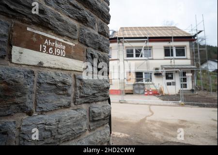 02. Januar 2022, Rheinland-Pfalz, Altenahr: Eine Markierung zeigt den Pegel der Ahr-Flut am 13. Juni 1910. Im Hintergrund ist ein Haus zu sehen, das beim Hochwasser am 14. Juli 2021 beschädigt wurde. Foto: Sebastian Gollnow/dpa Stockfoto