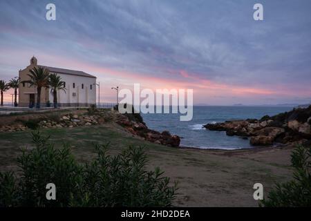 Mediterraner Sonnenaufgang mit beleuchteten Streifen Himmel. Ermita (Kapelle) de Nuestra Señora del Carmen. Isla Plana, in der Nähe von Puerto de Mazarrón, Murcia, Spanien Stockfoto