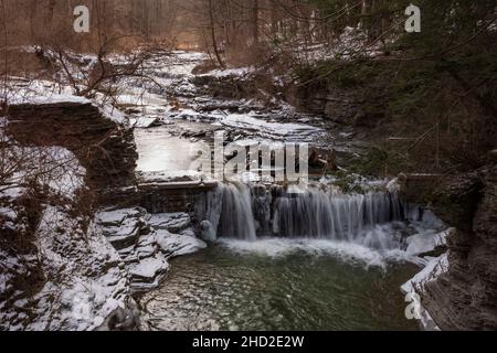 Das Wasser aus einem Bach stürzt an einem kalten Wintertag in einen kleinen Wasserfall im Buttermilk Falls State Park in Ithaca, NY. Stockfoto