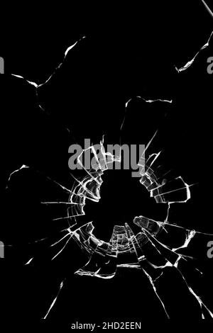 Struktur von Rissen am Fenster, gebrochenes Glas mit einem Loch auf schwarzem Hintergrund. Stockfoto