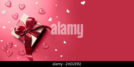 Valentinstag Dekorationen weiße Geschenkbox mit rotem Band Schleife und kleinen Herzen auf isoliertem roten Hintergrund mit leerem Raum. Stockfoto