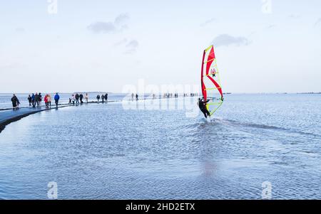 Wanderer, die am 1. Januar 2022 am Rand des Marine Lake in West Kirby fotografiert wurden, als ein Windsurfer auf dem Wirral auf dem Wasser abzieht. Stockfoto