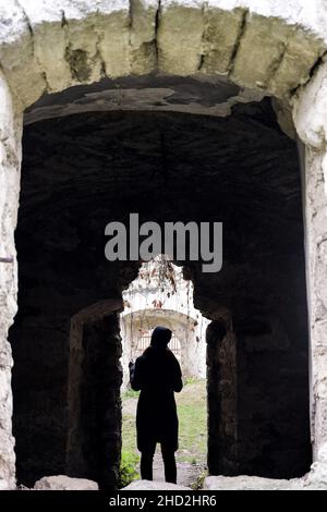 Silhouette eines jungen Mädchens in der Tür einer verfallenen alten Synagoge.Blick durch ein Bogenfenster. Rashkov, Moldawien. Nahaufnahme. Selektiver Fokus Stockfoto