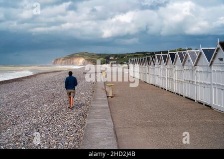 Hautot sur Mer, Frankreich - 30. Juli 2021: Männer laufen auf leerstem Sandstrand mit weißen Badeboxen aus Holz in Hautot sur Mer Stockfoto