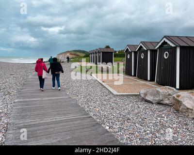 Hautot sur Mer, Frankreich - 30. Juli 2021: Menschen, die bei Regenwetter am Sandstrand von Sainte Marguerite mit hölzernen Badekisten spazieren Stockfoto