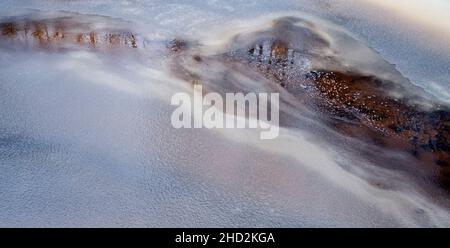 Verspielte Farben auf schneebedeckten und eisbedeckten Flüssen in Nahaufnahme Stockfoto