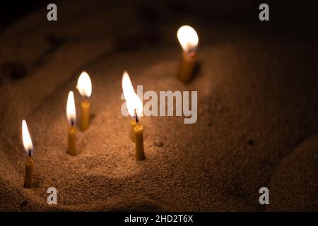 Verstreute Kerzen, die mit einem goldgelben Licht im Sand leuchten, kopieren den Raum Stockfoto