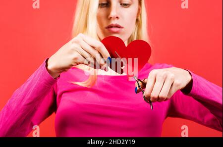 Mädchen mit gebrochenem Herzen. Beziehungsbruch. Traurige Frau schneidet herzförmiges Papier. Selektiver Fokus Stockfoto