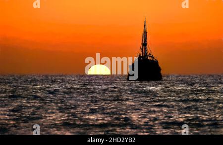 Piratenschiff Ocean Sunset Silhouette ist ein altes hölzernes Piratenschiff mit vollen Flaggen, wenn die Sonne am Ozeanhorizont in einem bunten Sonnenuntergangshimmel untergeht Illustr Stockfoto