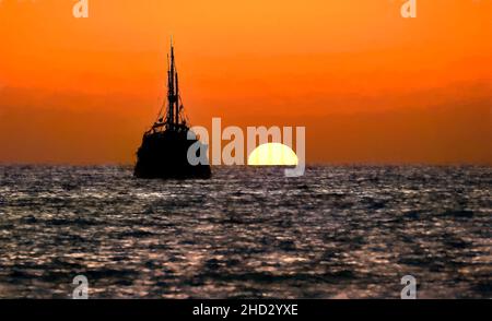 Piratenschiff Ocean Sunset Silhouette ist ein altes hölzernes Piratenschiff mit vollen Flaggen, wenn die Sonne am Ozeanhorizont in einem bunten Sonnenuntergangshimmel untergeht Illustr Stockfoto