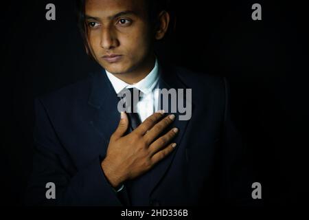 Nahaufnahme eines hübschen indischen Mannes, der einen eleganten Anzug mit Krawatte auf schwarzem Hintergrund trägt Stockfoto