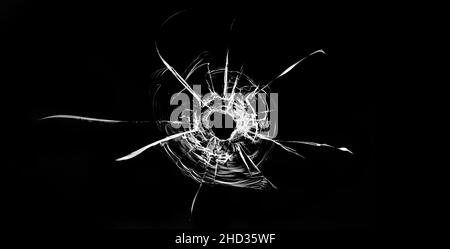 Risse im Fenster. Einschussloch im Glas. Isoliert auf schwarzem Hintergrund. Stockfoto