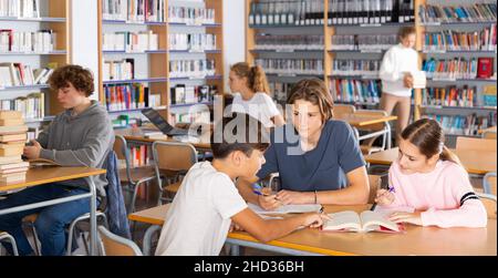 Gruppe von Schulkindern, die gemeinsam Bücher in der Bibliothek lesen und sich auf die Schulprüfung vorbereiten Stockfoto