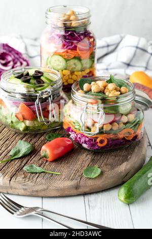 Nahaufnahme von hausgemachten Salatgläsern, serviert auf einem rustikalen Holzbrett. Stockfoto