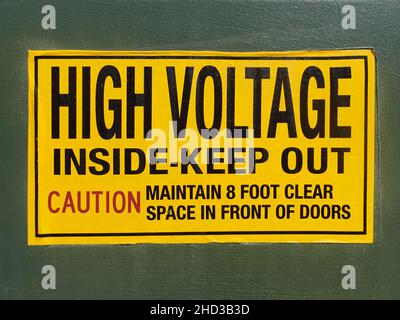 Ein schwarzes auf gelbem Hochspannungswarnschild an der Seite des Transformatorgewölbes. Stockfoto