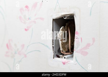 Freiliegende Steckdose an der Wand, die ein Sicherheitsrisiko darstellt, selektiver Fokus. Stockfoto