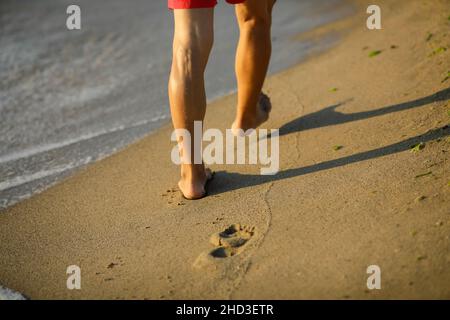 Details zur geringen Schärfentiefe (selektiver Fokus) mit einem Mann, der an einem ruhigen und warmen Sommermorgen am Schwarzen Meer im OBZ barfuß im Sand läuft Stockfoto