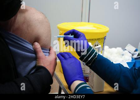 Ein Mitarbeiter des Gesundheitsdienstes (National Health Service) verabreicht einem Mann in einem Impfzentrum einen Pfizer/BioNTech Covid-19-Auffrischungsimpfstoff. Stockfoto