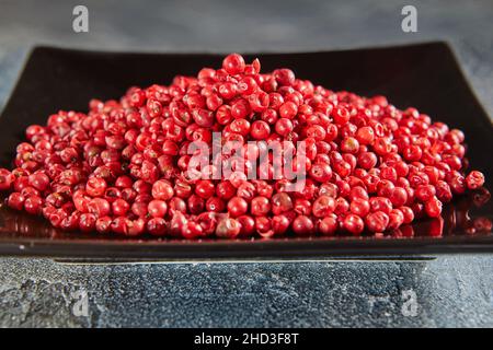 Rote Pfefferkörner auf schwarzem Teller mit Spiegelung Stockfoto
