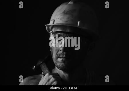 Miner-Gesicht auf schwarzem Hintergrund. Kopf müde Bergmann in Helm und Brille. Schwarzweiß-Porträt Stockfoto