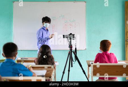 Lehrer in medizinischer Maske mit begrenzten Kindern Unterricht und Streaming Live-Klassen an Schüler im Klassenzimmer während Coronavirus covid-19 pendamic - Konzept Stockfoto