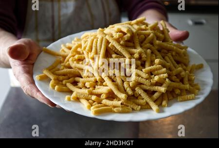 Omas Hände halten einen Teller mit rohen, hausgemachten Passatelli. Traditionelle italienische Pasta in Brühe gekocht. Stockfoto