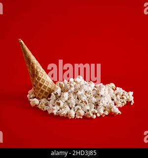 Umgedrehter Eiszapfen mit verschüttetem Popcorn auf rotem Hintergrund. Minimales kreatives Stillleben-Food-Konzept. Stockfoto