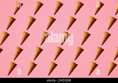 Eiscreme-Waffelkegel mit sich wiederholendem Muster auf rosa Hintergrund. Minimalistisches Stillleben kaltes Sommeressen Konzept. Flach liegend. Stockfoto