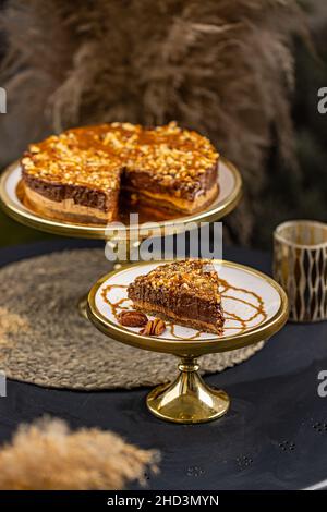 Stillleben von Schokoladenkuchen mit Nüssen und gesalzenem Karamell auf Kuchenständer Stockfoto