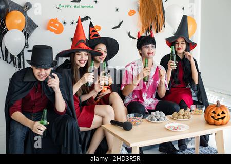 Bande von jungen Asiaten in Kostüm Hexe, Zauberer mit feiern Halloween-Party zum Tanzen und Trinken und betrunken im Zimmer. Gruppe teen Thai mit feiern Stockfoto