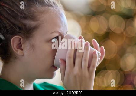 An heiligabend trinkt eine junge Frau mit Dreadlocks Kaffee drinnen. Stockfoto