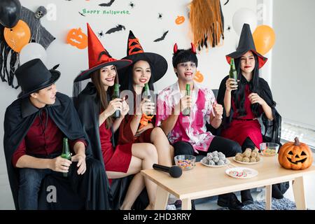 Bande von jungen Asiaten in Kostüm Hexe, Zauberer mit feiern Halloween-Party zum Tanzen und Trinken und betrunken im Zimmer. Gruppe teen Thai mit feiern Stockfoto