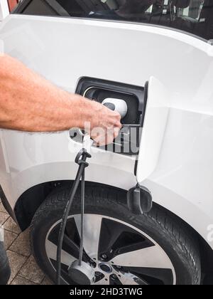 Ein Mann, der Ladegerät in sein weißes Elektroauto setzt Stockfoto