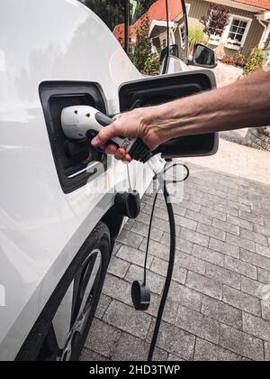 Ein Mann, der Ladegerät in sein weißes Elektroauto setzt Stockfoto